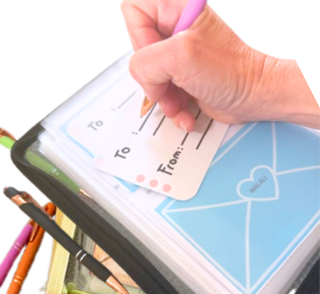 Hand holding a pen over a set of personalized cards with 'To' and 'From' fields, surrounded by additional pens.